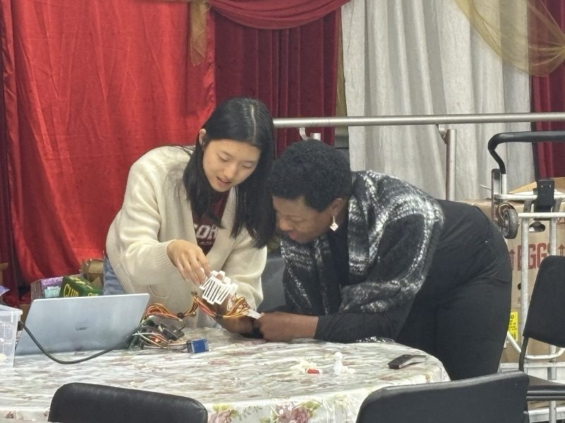 Yanzi and a resident leaning over the device together at a table, laptop open beside them